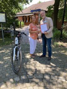 Der Kaufmännische Direktor Thomas Job überreicht den Gutschein für eine Wochenend-Radtour mit zwei Dienst-Pedelecs an Danuta Mrozek von Gliszcynski, Mitarbeiterin in der Küche der LWL-Klinik Herten.<br>Foto: LWL/Sommer
