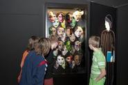 Besucher schauen sich die Masken in der Ausstellung an.  (vergrößerte Bildansicht wird geöffnet)