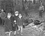 Vorbeimarsch der deutschen Ortsbevölkerung an den ermordeten und auf Befehl der 95. Infanterie-Division exhumierten Zwangsarbeiter in Suttrop. Fototext: "German mother shields eyes of son as she walks with other civilians past row of exhumed dead Russians outside town of Suttrop. A common grave contained bodies of 57 Russians shot and killed by Nazis. Among victims were women and one infant child. Recovery of bodies was done under Supervision of 95th Infantry Division of U.S. Ninth Army", Freigabe durch den Field Press Censor am 05.05.1945. / NARA, Washington