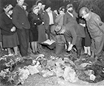 Durchsuchung der Leichen der durch Genickschuss ermordeten Zwangsarbeiter nach Personalpapieren, Suttrop. "Members of the U.S. Ninth Army occupying Suttrop, Germany, were led by informers to a huge common grave containing bodies of 57 Russians including many women and one baby, who were forced to dig their own grave, made to kneel at the edge of it so that their dead bodies fell into the grave when they were shot. German civilians were made to exhume bodies on orders of American officers so that with the aid of Russian displaced persons the victims could be identified, and then made to rebury them in individual graves. Here a German civilian gives information he has just taken from a corpse to a captain of the 95th Infantry Div., for identification." Freigabe durch den Field Press Censor am 05.05.1945. / NARA, Washington