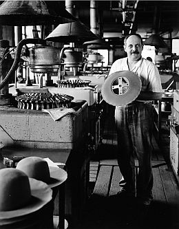 Das historische Schwarz-Weiß-Foto zeigt einen Mann beim Formziehen eines Hutes in der Hutfabrik.